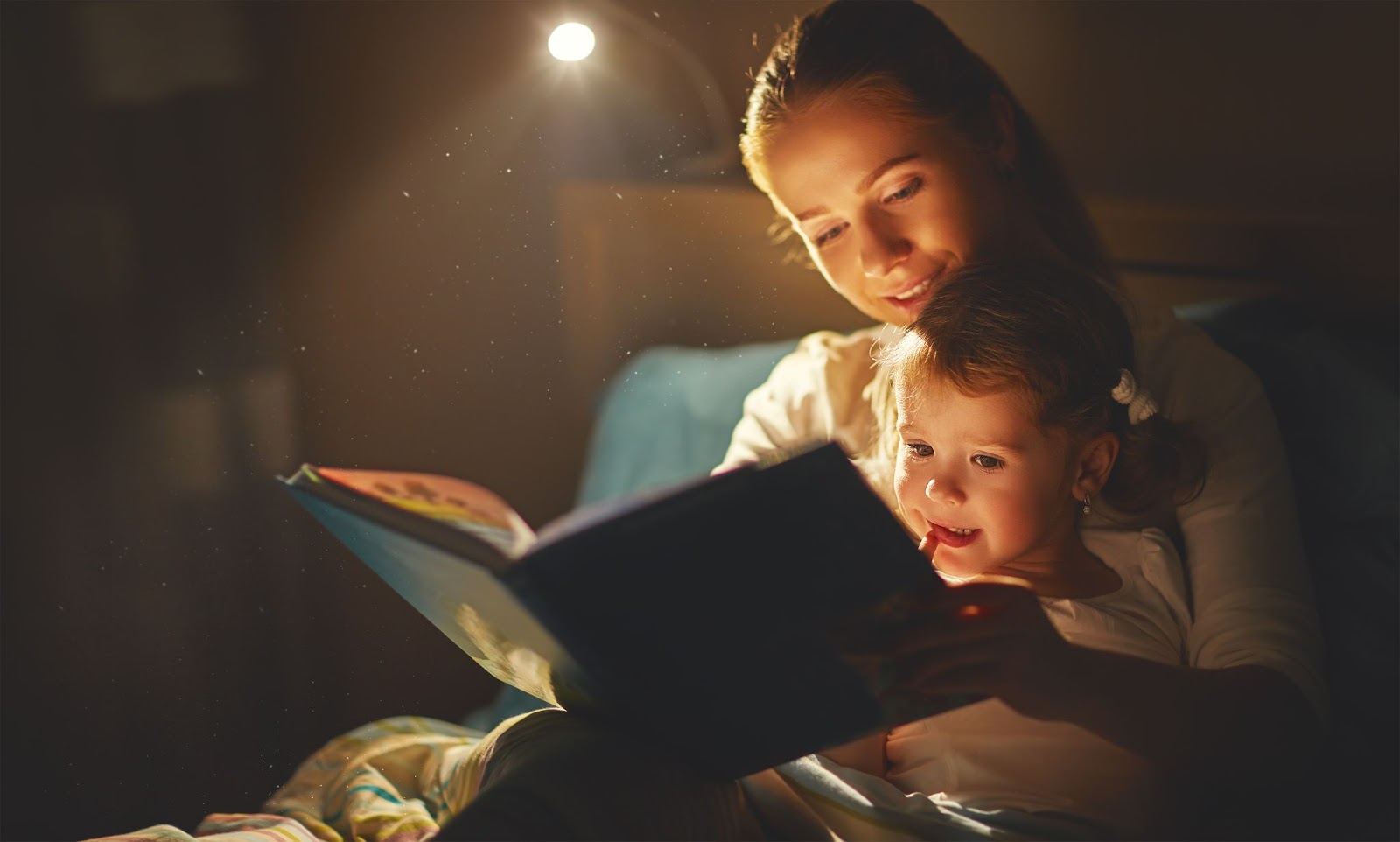 читает дочке книгу, чтобы научить ребенка засыпать самостоятельно